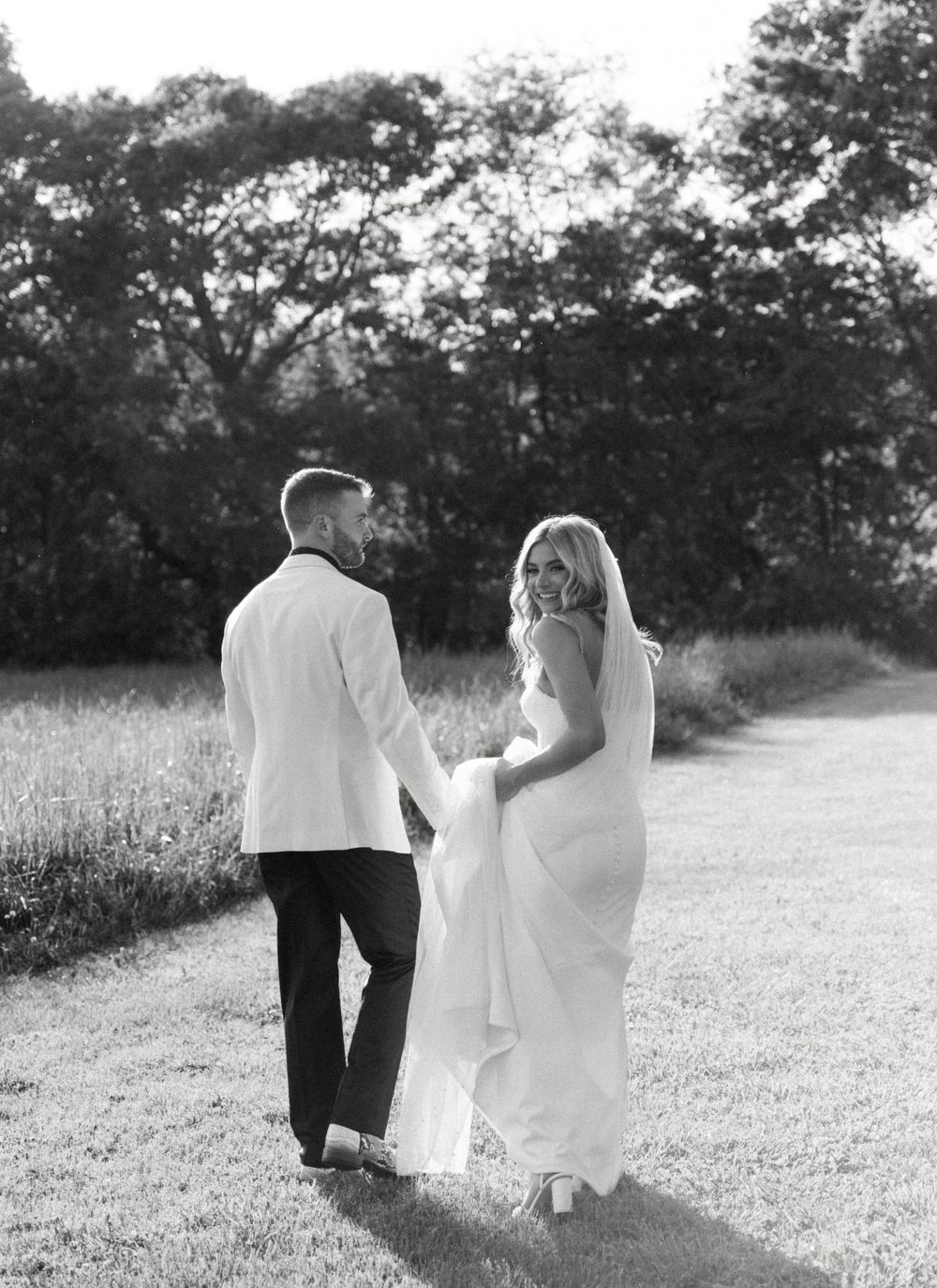 A black and white photo series shows a couple walking away together on a country path through fields and trees.