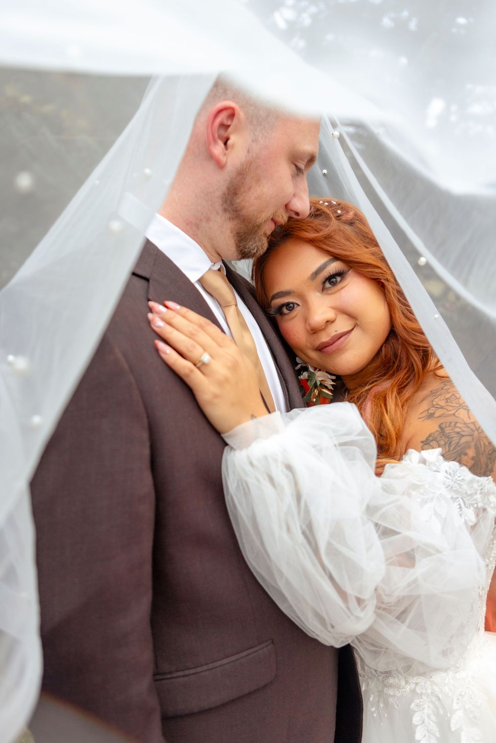Wedding couple shares tender moments while embracing under a delicate white veil in winter setting.