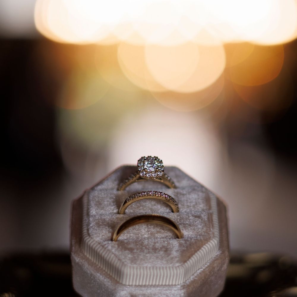 Close-up photo of an engagement ring with diamonds on a textured white surface in soft bokeh lighting.