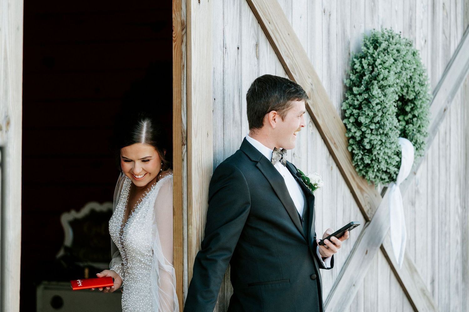 A couple in formal wedding attire stands together against a white wooden wall during their special day.