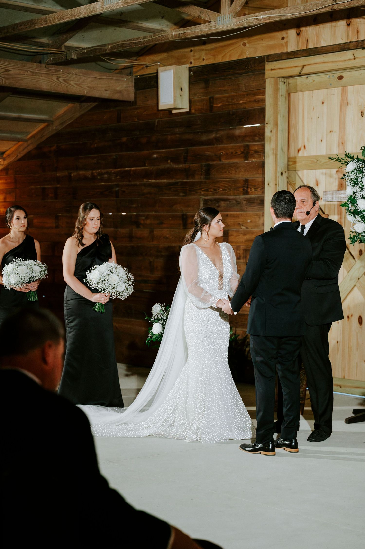 Wedding party members in formal attire gather in a rustic wooden barn venue for photos.