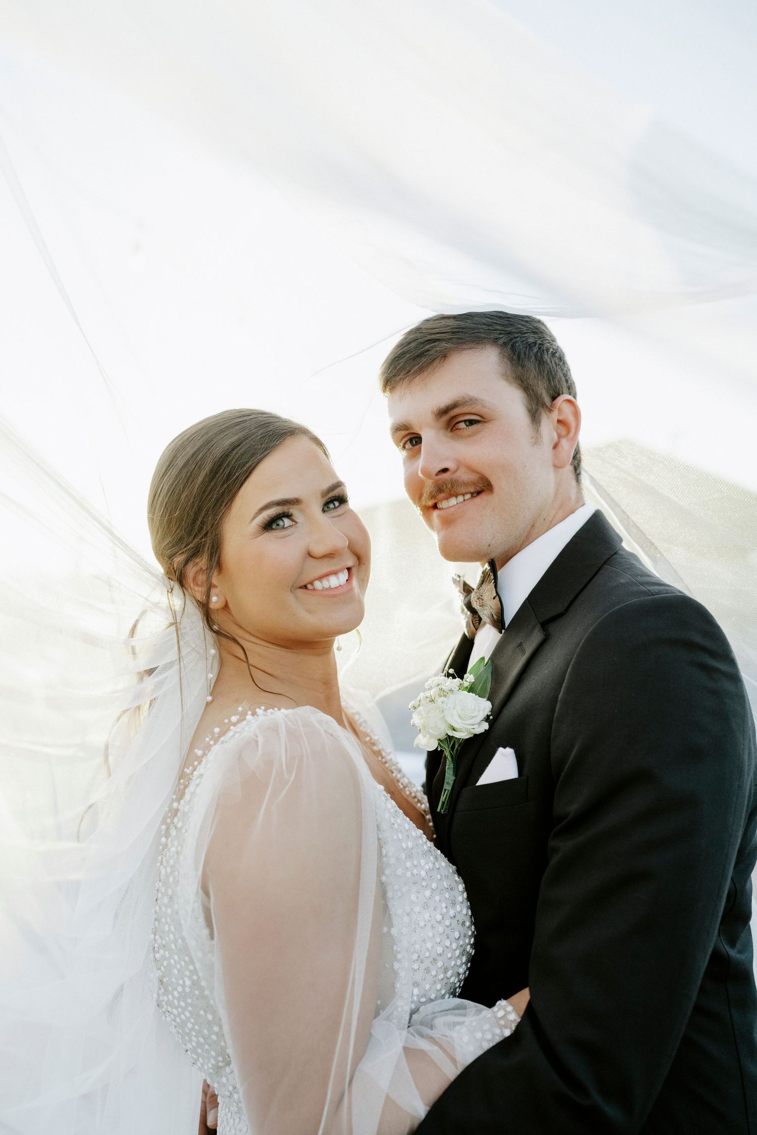 A tender moment between newlyweds as they pose together in traditional wedding attire with soft lighting.