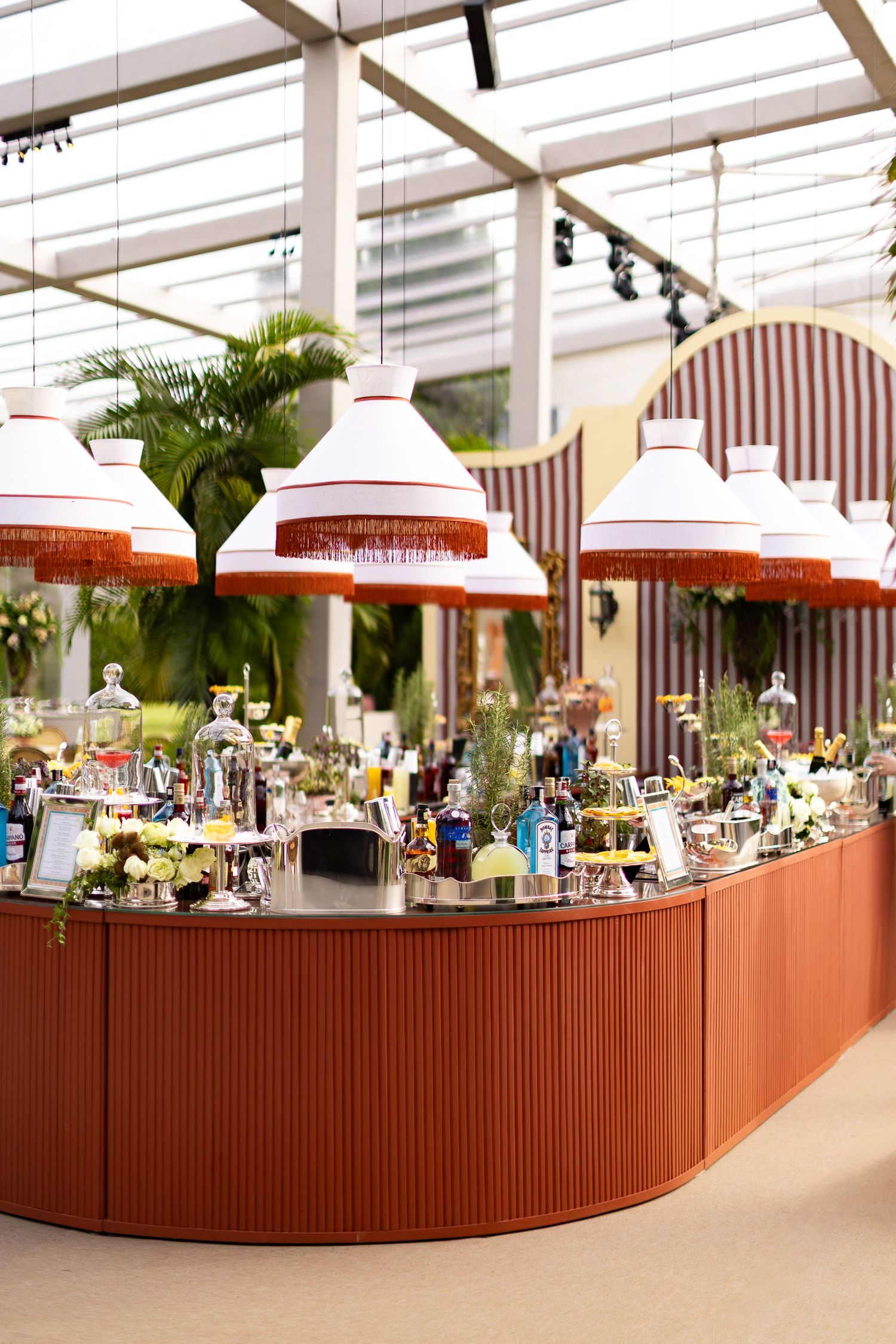Elegant bar setup with white and orange fringed lampshades and decorative glassware displays in an upscale event space.