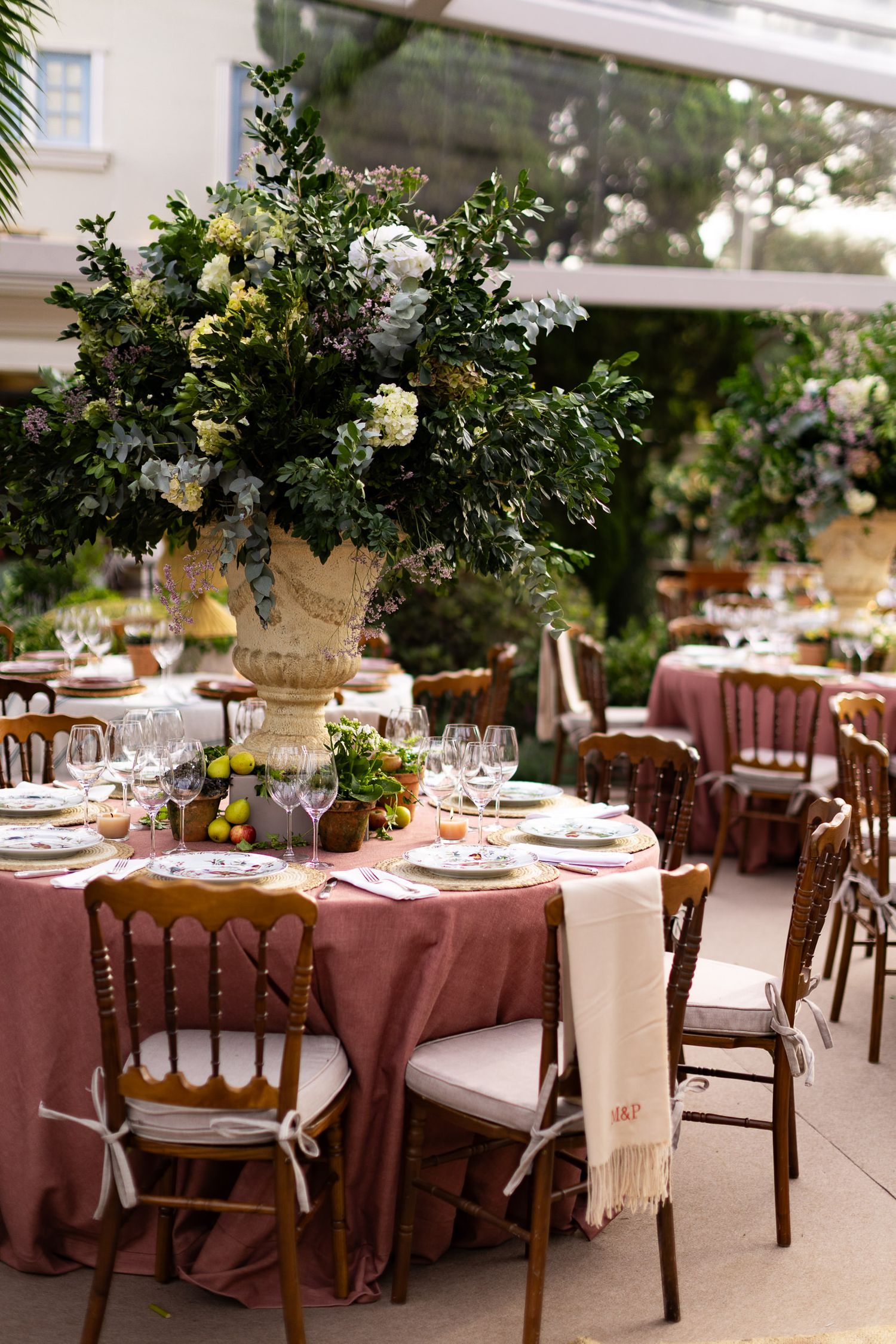 Elegant wedding reception tables with dusty rose linens and lush floral centerpieces in an outdoor garden setting.