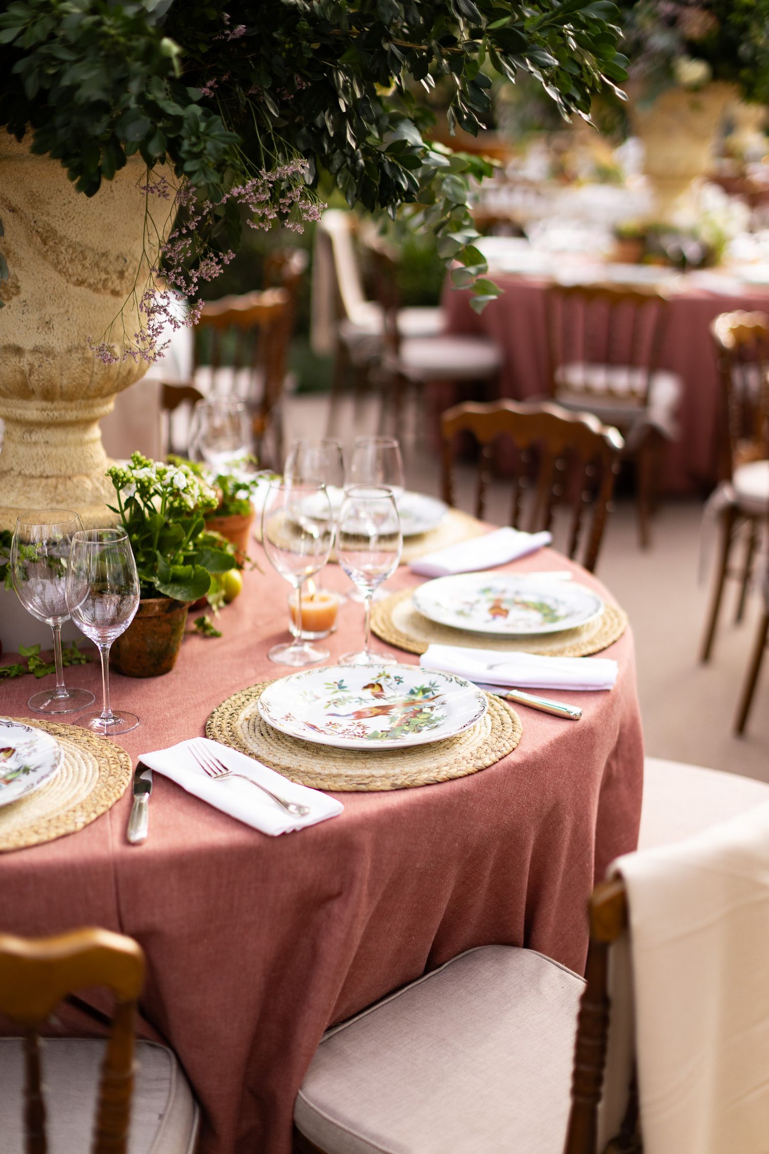 Elegant table settings with burgundy tablecloths, white plates, and greenery decorations at a formal dining event.