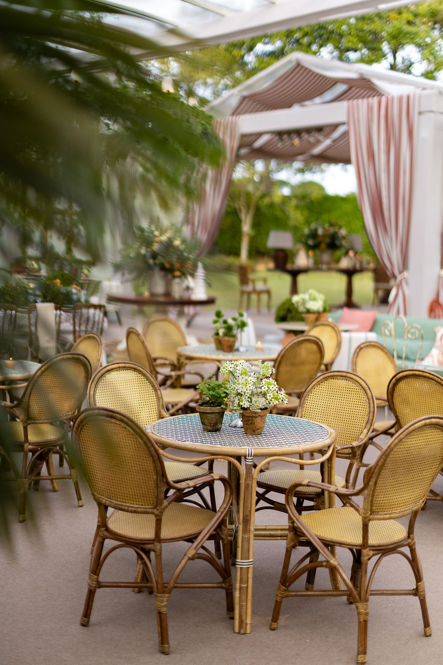Elegant outdoor seating area with rattan chairs and round bistro tables arranged on a covered patio.