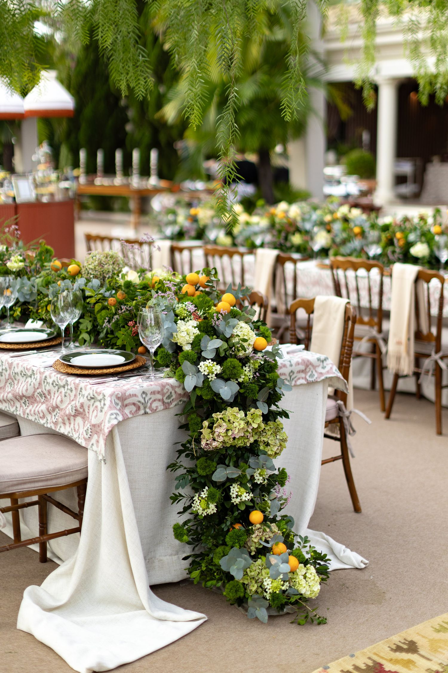 Elegant wedding reception tables decorated with white linens, floral centerpieces featuring yellow and green blooms, and wooden chairs.