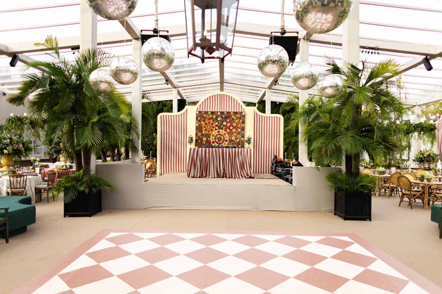 Elegant event venue with pink and white checkered dance floor, hanging plants, and vintage-style stage backdrop.