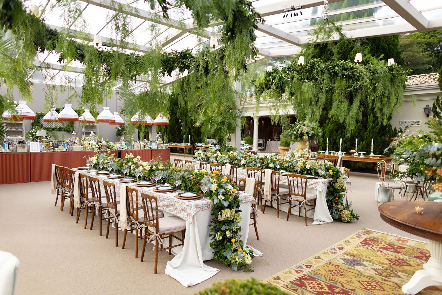 A lush greenhouse wedding venue decorated with hanging greenery and white chairs arranged for a ceremony.