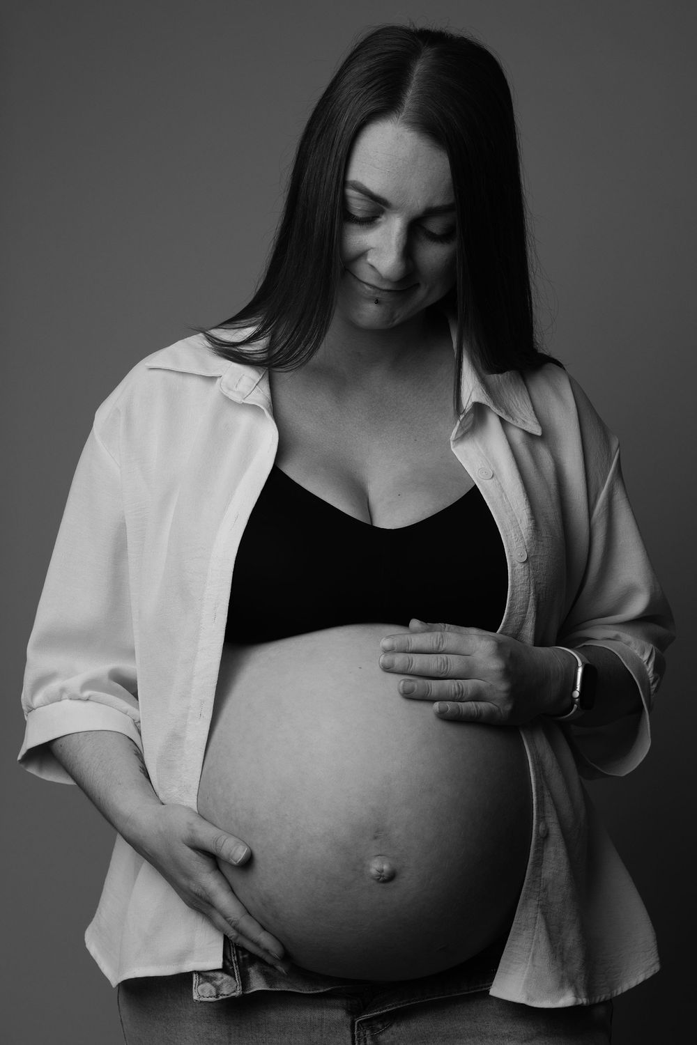 Black and white image of a mother looking down at her baby bump during a maternity session in Ceredigion