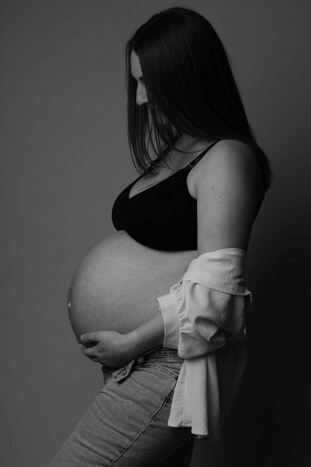 Black and white image of a pregnant mother looking down at her baby bump during a maternity photoshoot in West Wales