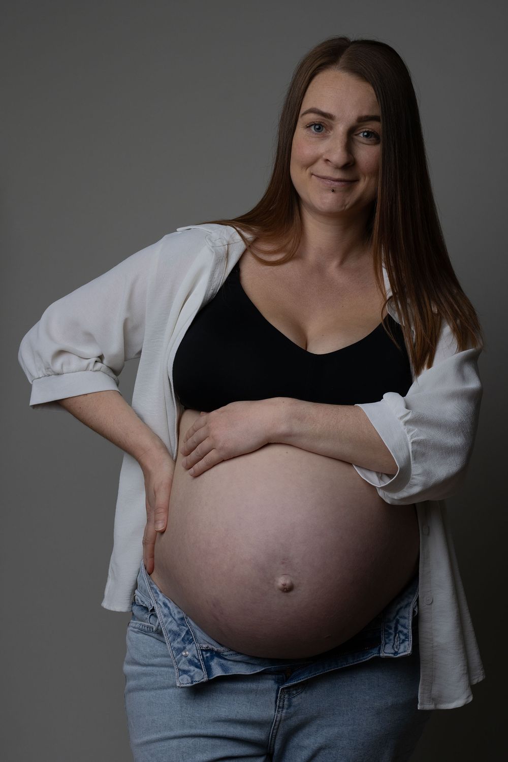 A mother wearing a white shirt and blue jeans during a maternity photoshoot with Ceris Hicks Photography