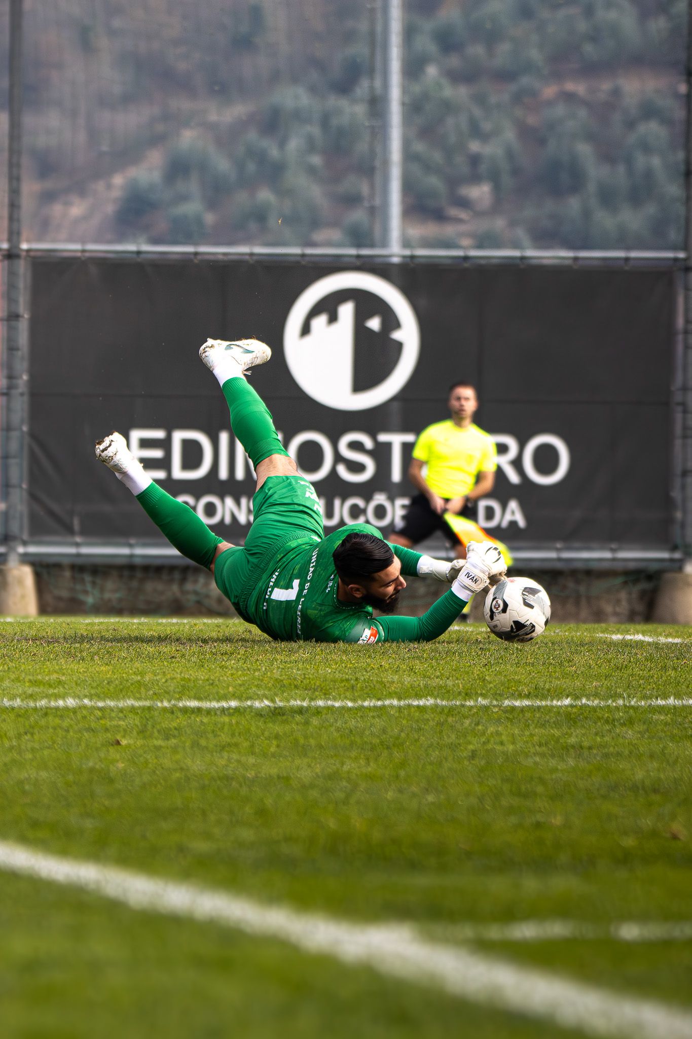 Soccer goalkeeper in green uniform diving to make a save during match on grass field.