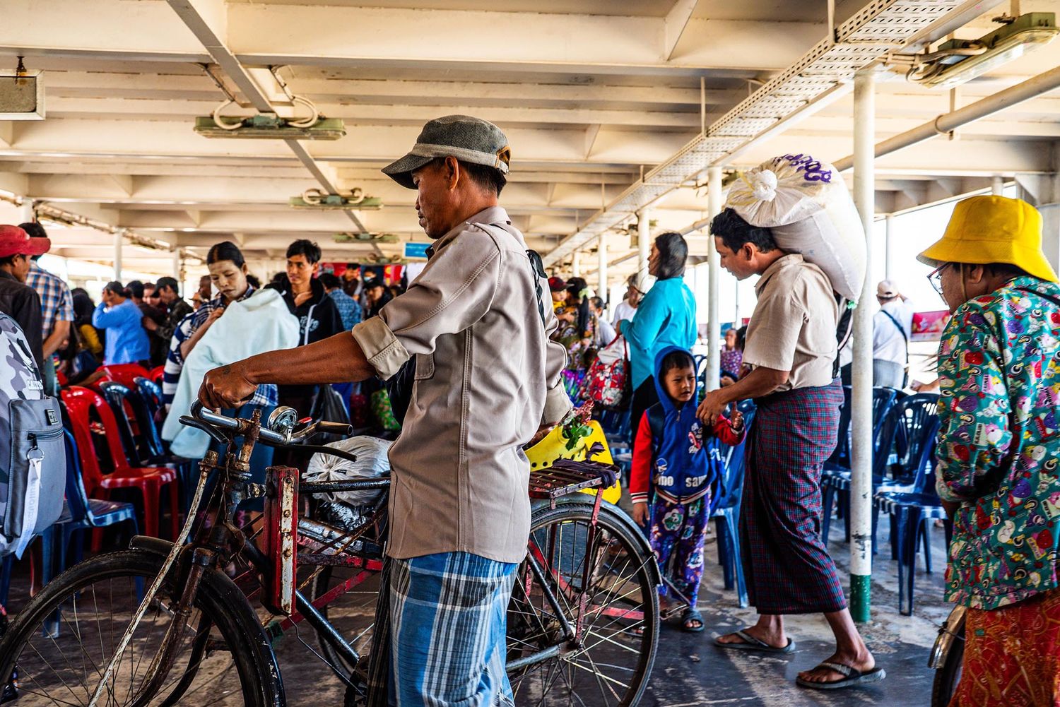 People wait in line with bicycles at a crowded ferry terminal in a coastal city.