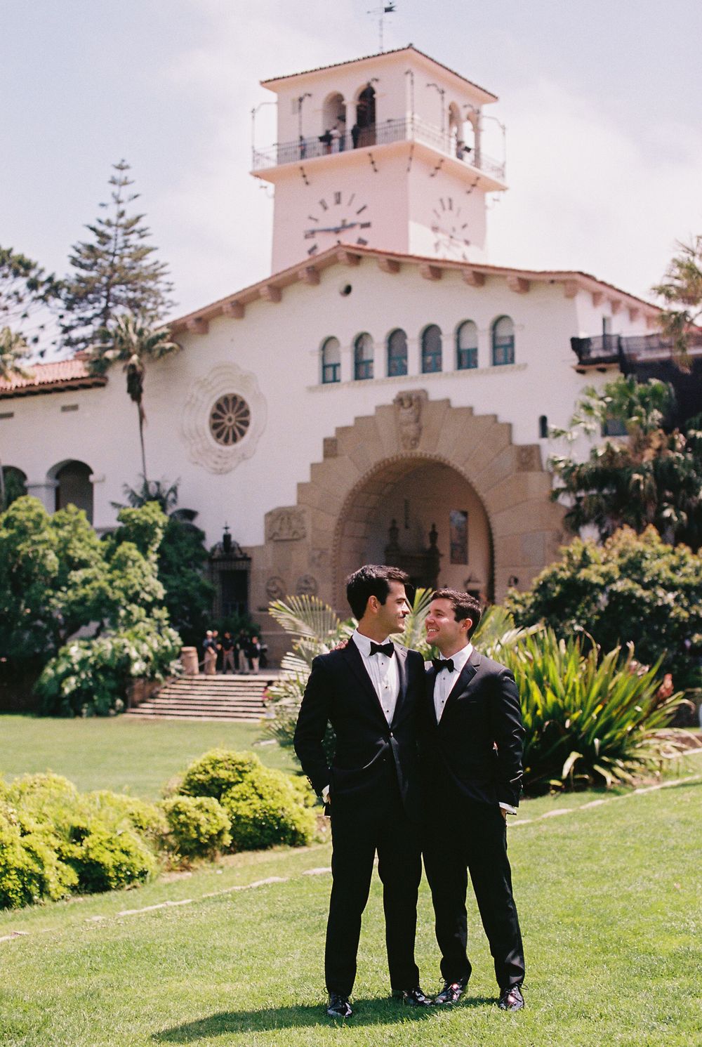 A 35mm film photo of the iconic Santa Barbara bell tower standing behind two grooms from Louisiana at the Santa Barbara county courthouse
