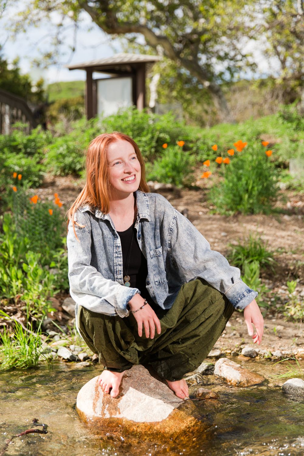 Person sitting on rock by stream in garden with orange flowers in background.