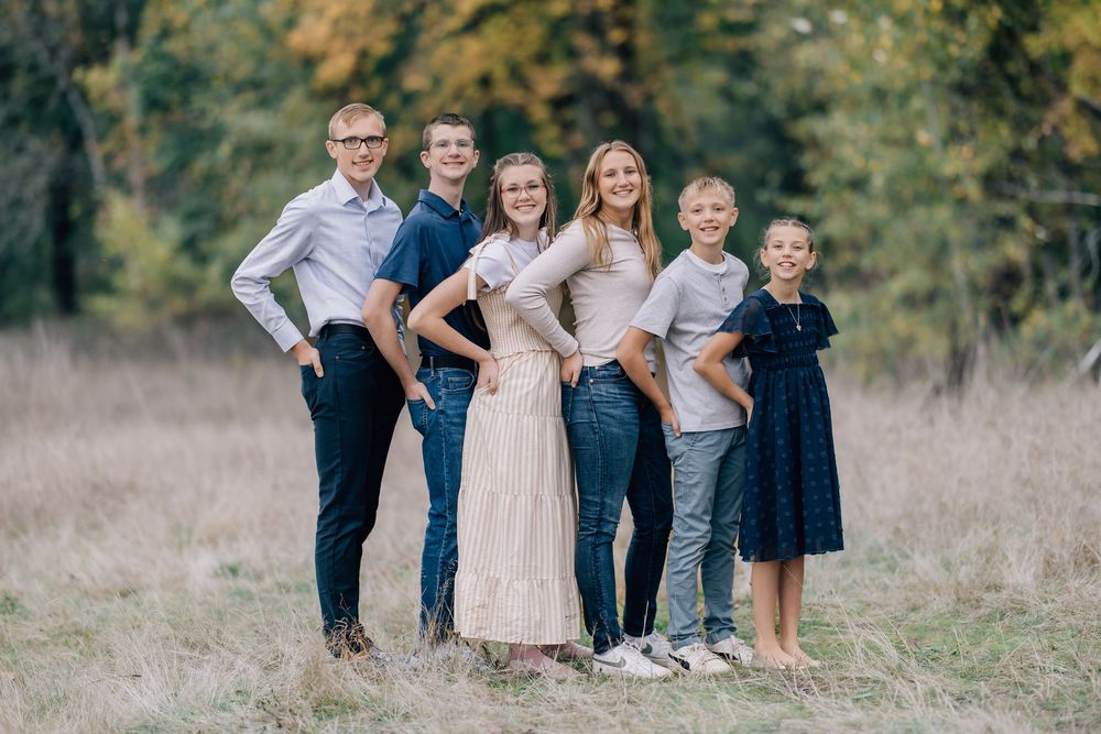 Six siblings pose together smiling in a golden field surrounded by autumn trees.