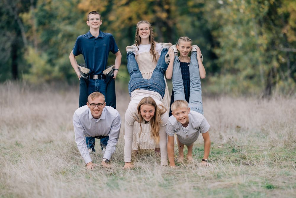 Fun family photo with parents doing push-ups while kids sit on their backs outdoors.