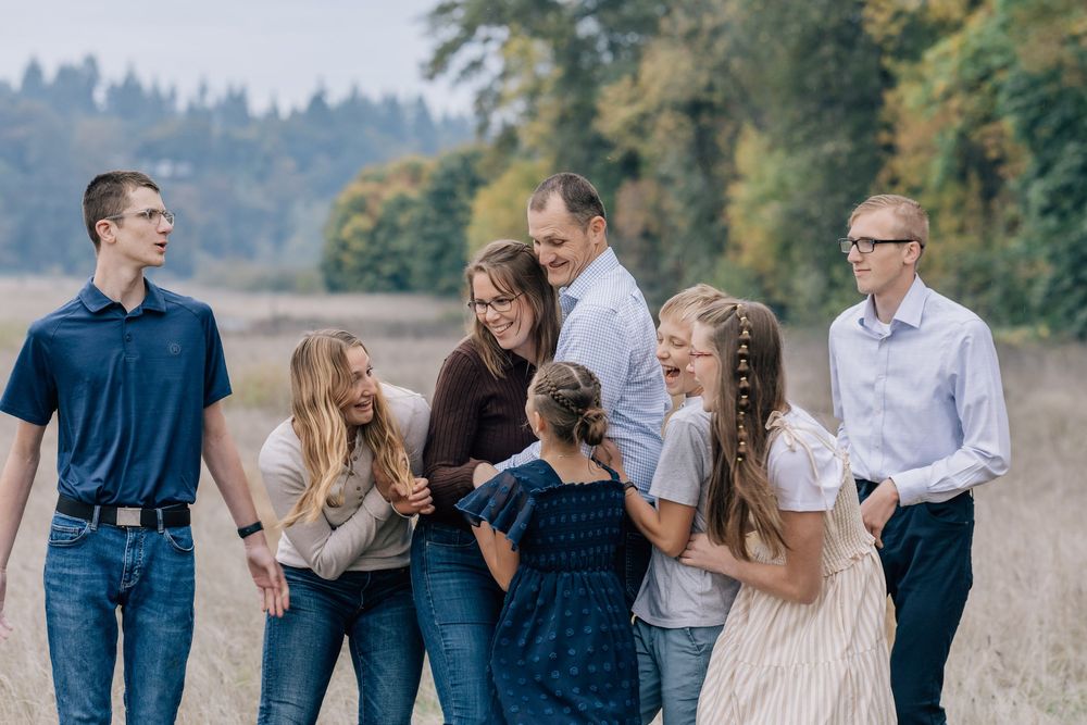 A family of seven shares a candid laughing moment together in an open autumn field.