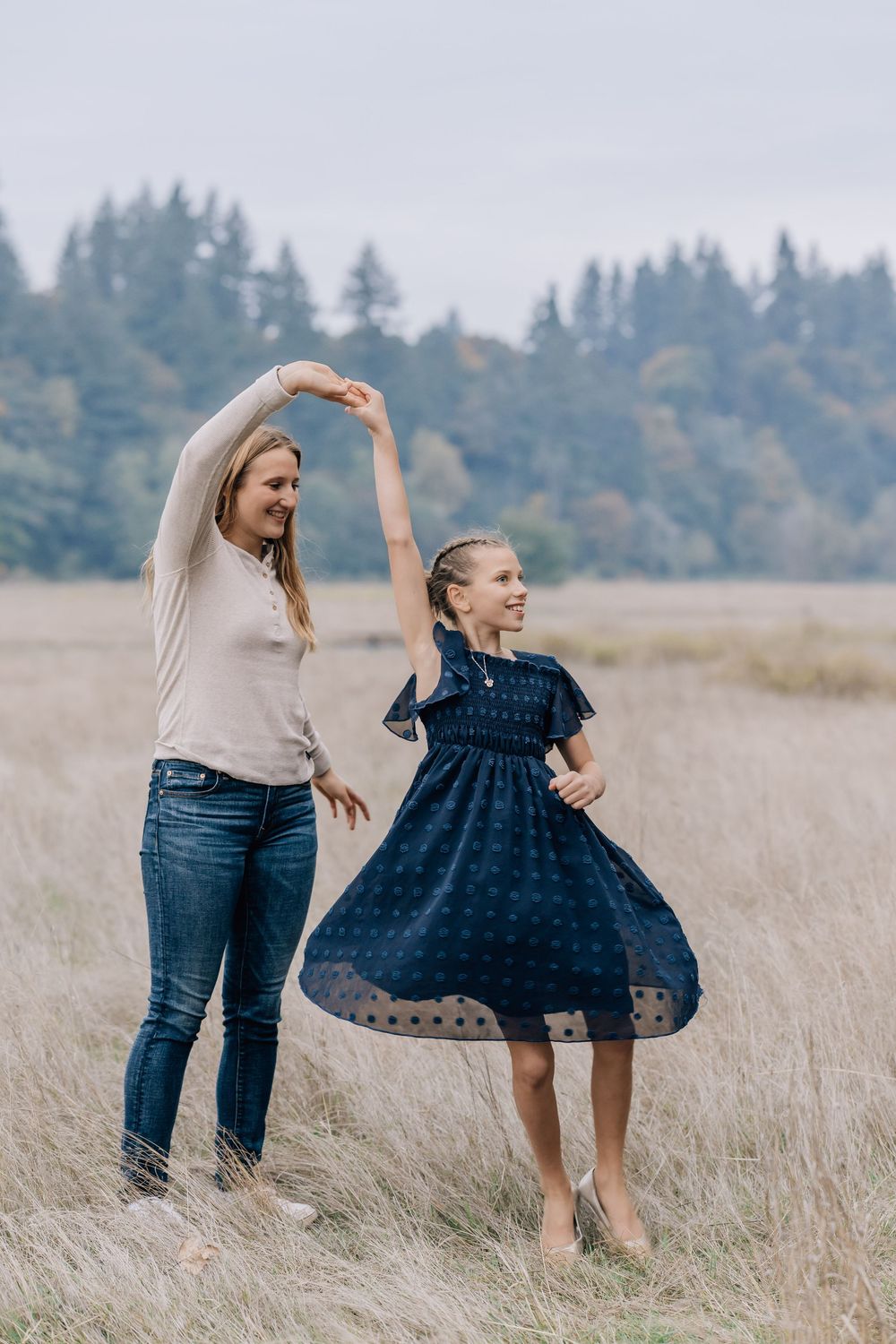 A mother and daughter dance together in a golden field, the girl wearing a navy dress.
