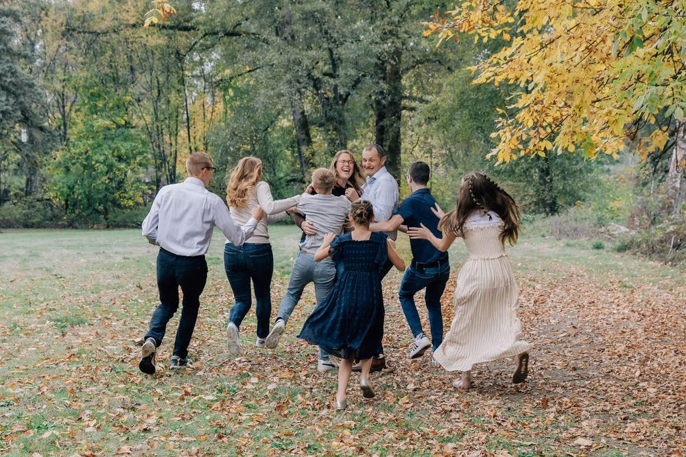 A large family runs and plays together in a leaf-covered autumn outdoor setting.
