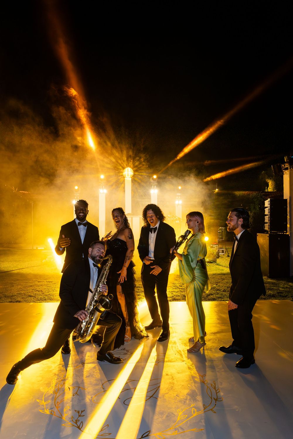 Wedding party guests dance and cast dramatic shadows on a dance floor illuminated by warm golden lighting.