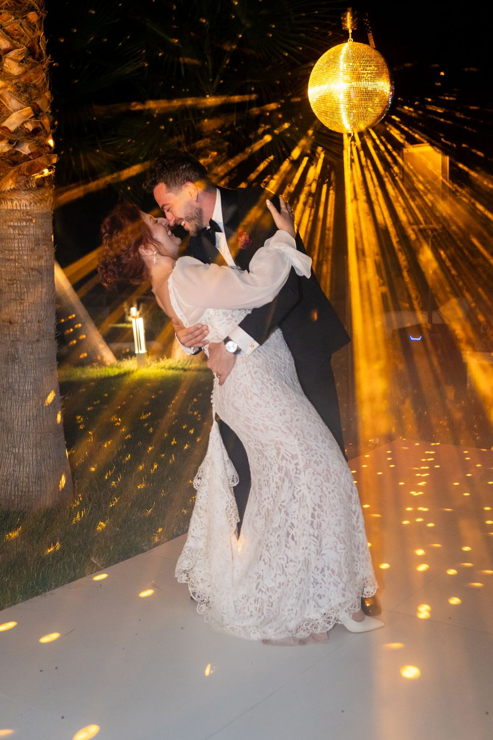 A couple dances on a white floor under dramatic golden disco lighting and sparkling effects at a wedding reception.