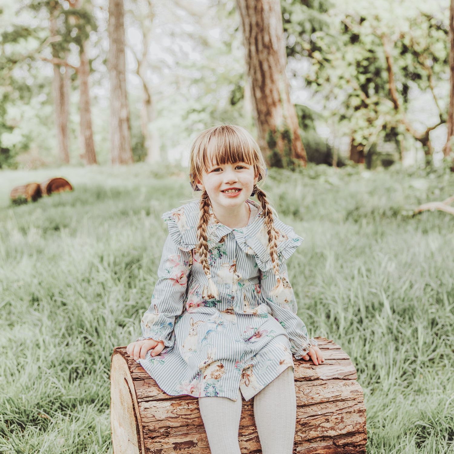 Young girl smiling in a woodland sitting on a log.