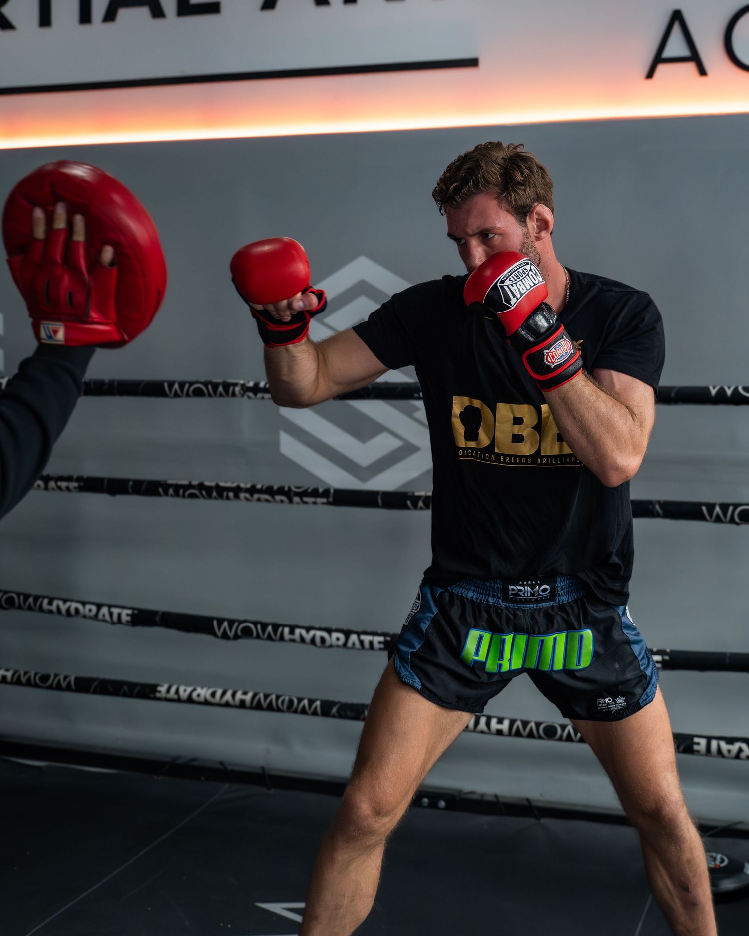 Fighter demonstrating boxing stance with red gloves against grey backdrop.