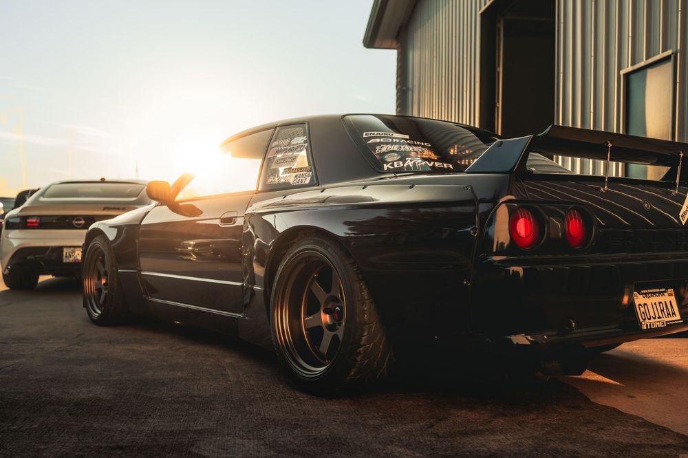 A black sports car photographed at sunset with dramatic lighting and reflective bodywork details.