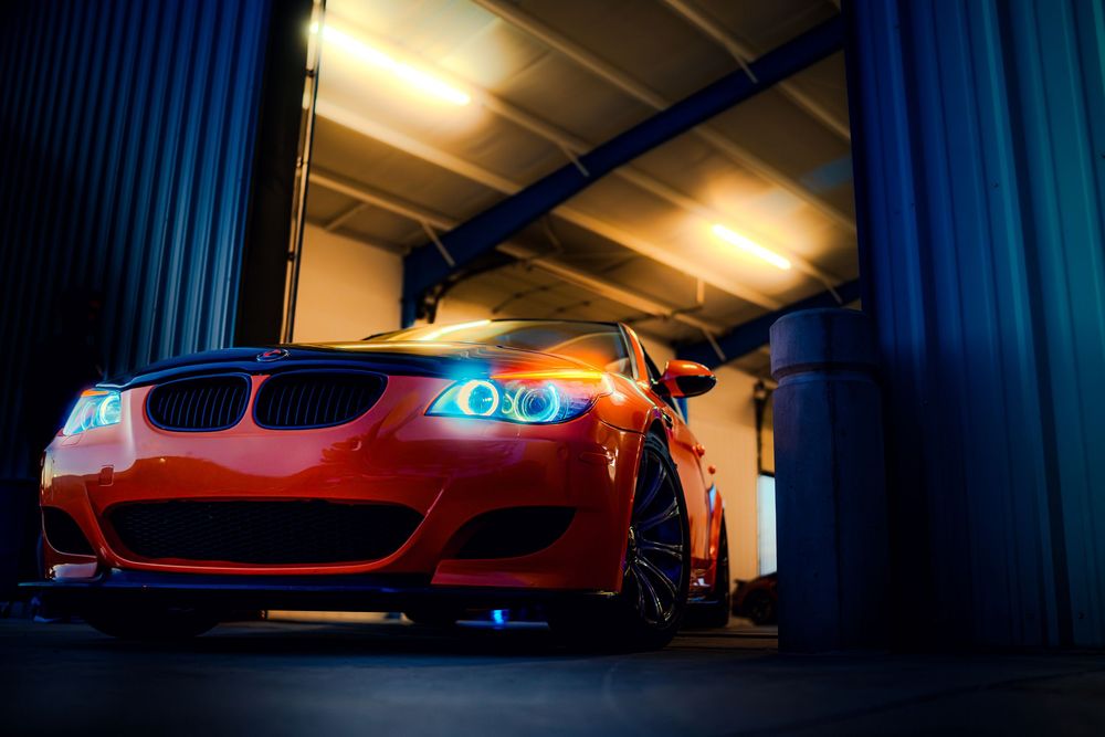 Red Ferrari sports car illuminated by dramatic lighting in a dark garage setting.