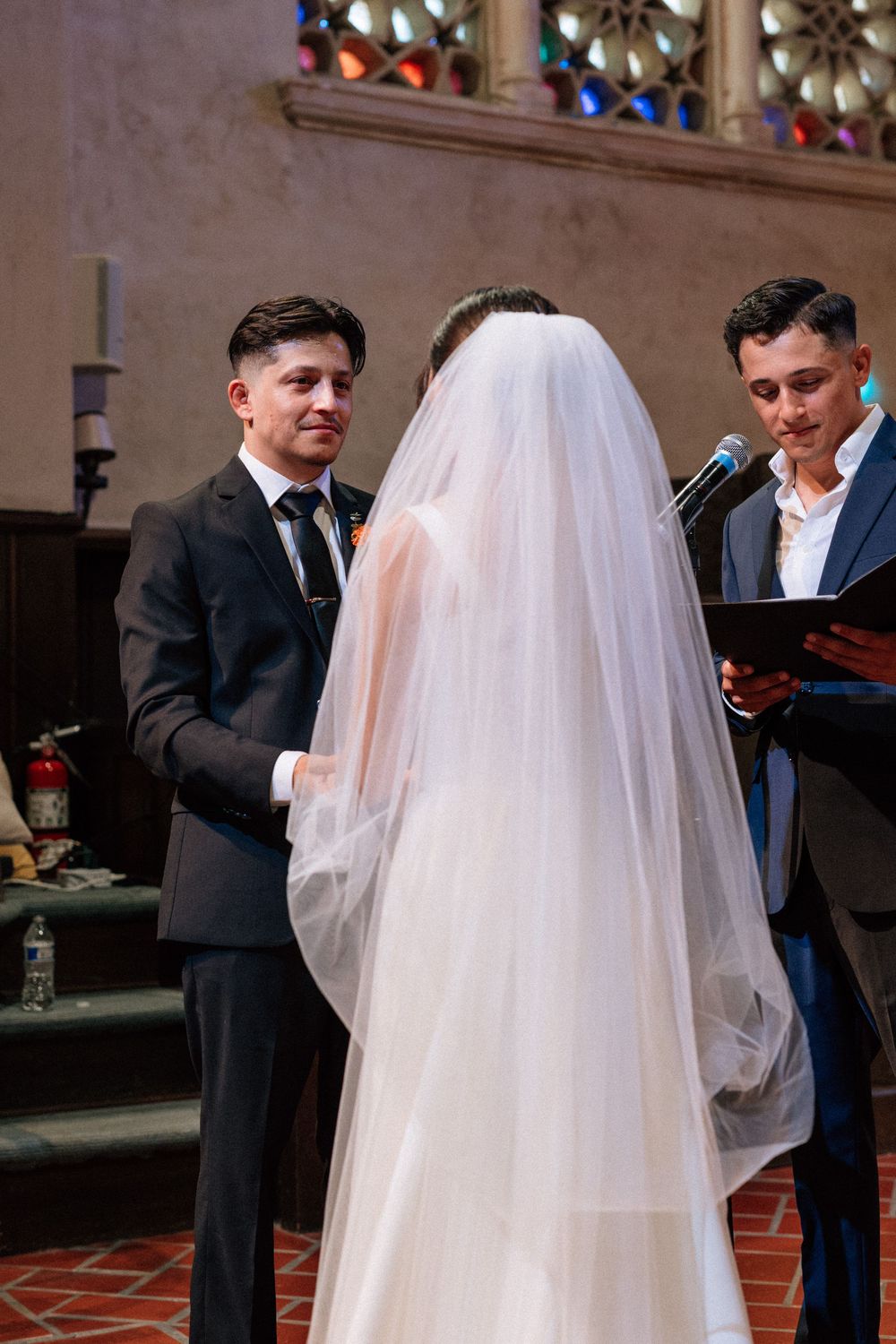 Detailed digital image by a Santa Barbara wedding photographer focusing on the emotional vow exchange and stained glass windows.