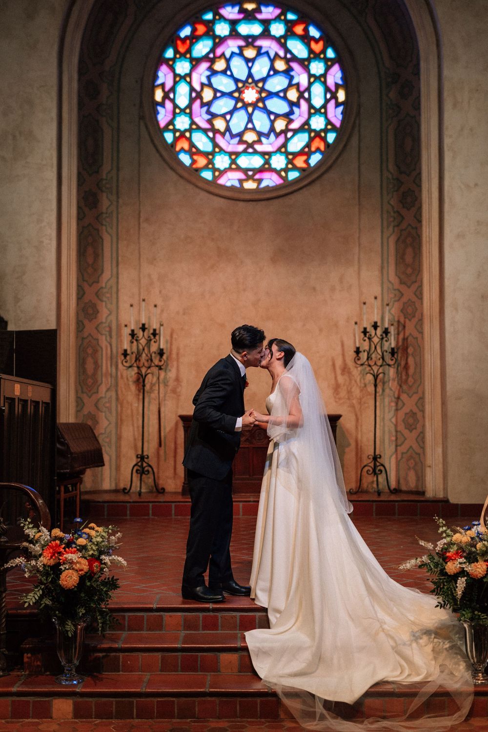 Artistic low-light film shot of a couple's first kiss under a stained glass window in Santa Barbara.