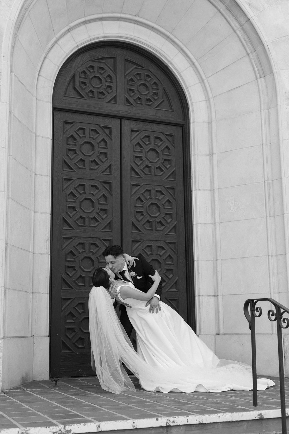 A black and white photo of a groom dipping a bride for an intimate kiss in front of the door at the Unitarian Society of Santa Barbara.