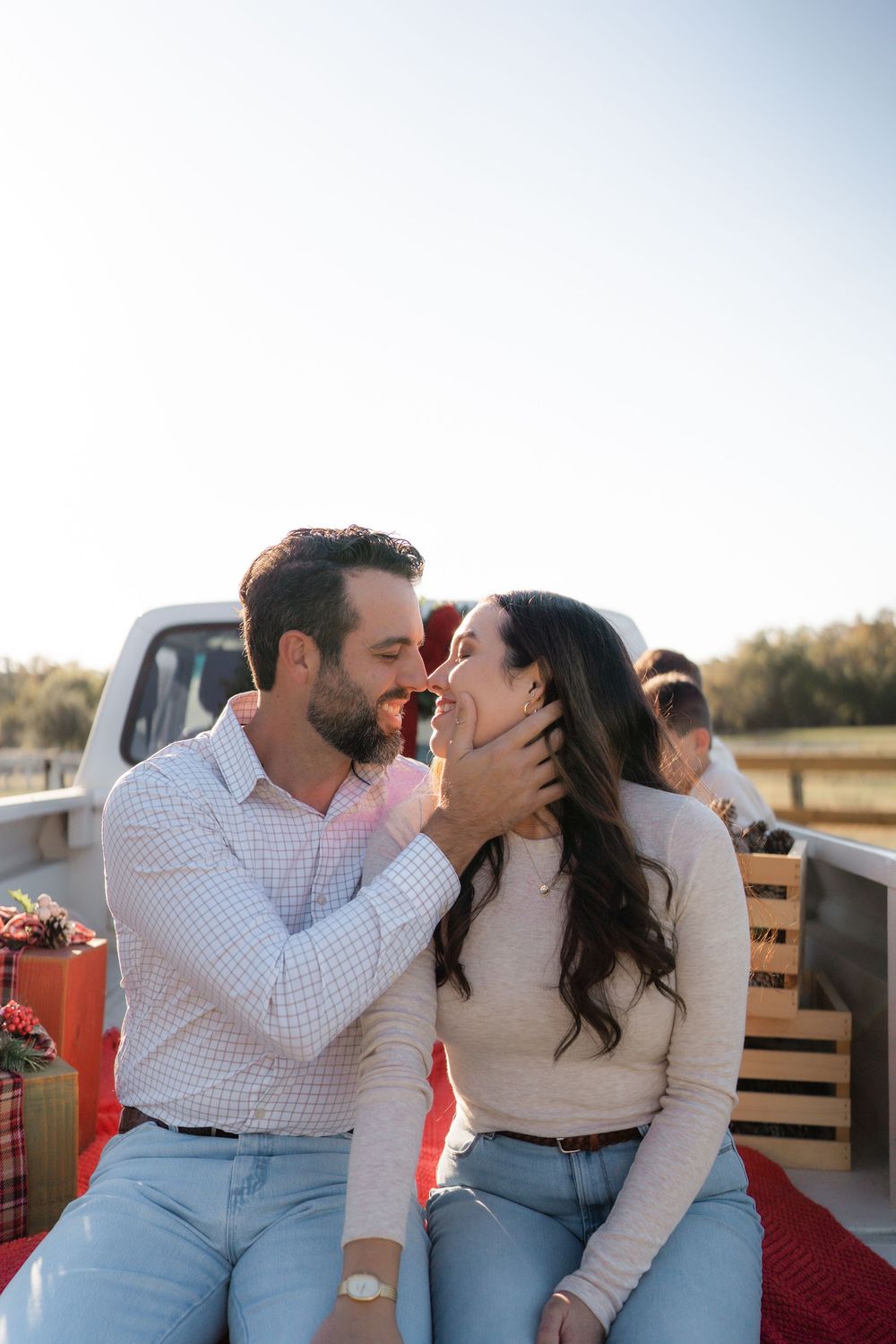Family enjoying a festive Texas farm Christmas mini session, sitting on the bed of an old red Ford truck decorated with holiday greenery.