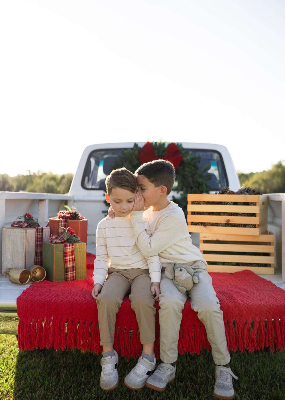 Family enjoying a festive Texas farm Christmas mini session, sitting on the bed of an old red Ford truck decorated with holiday greenery.