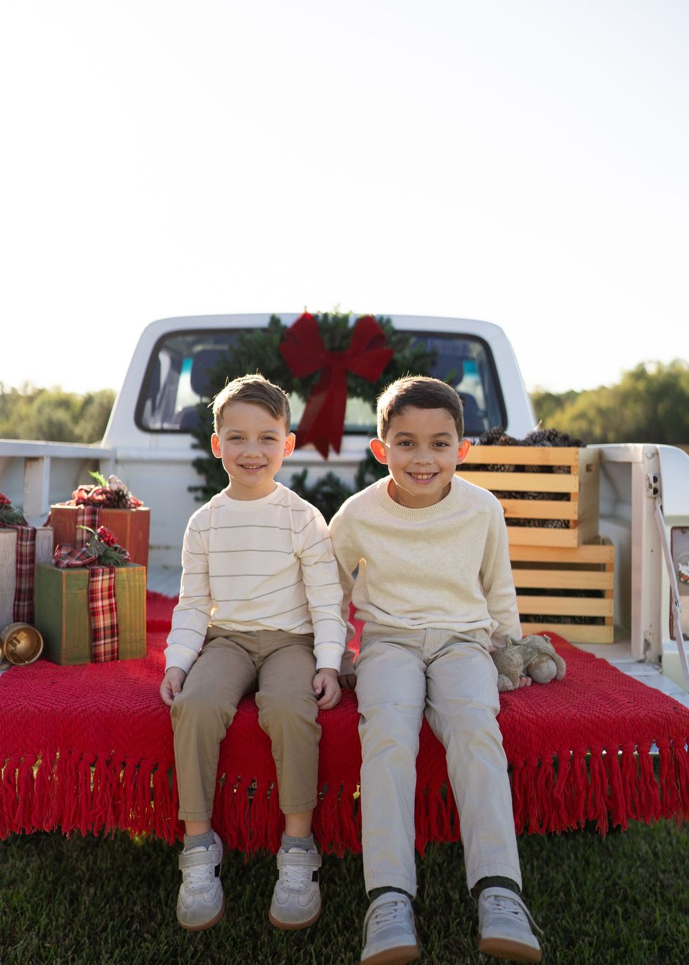 Family enjoying a festive Texas farm Christmas mini session, sitting on the bed of an old red Ford truck decorated with holiday greenery.