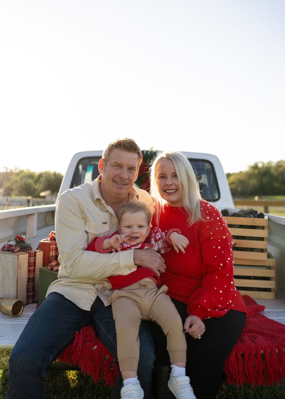 Family enjoying a festive Texas farm Christmas mini session, sitting on the bed of an old red Ford truck decorated with holiday greenery.