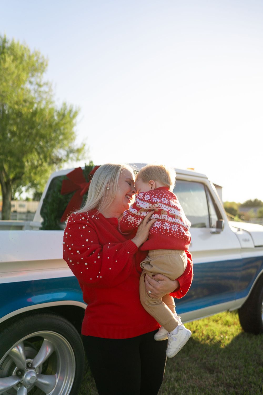 Family enjoying a festive Texas farm Christmas mini session, sitting on the bed of an old red Ford truck decorated with holiday greenery.