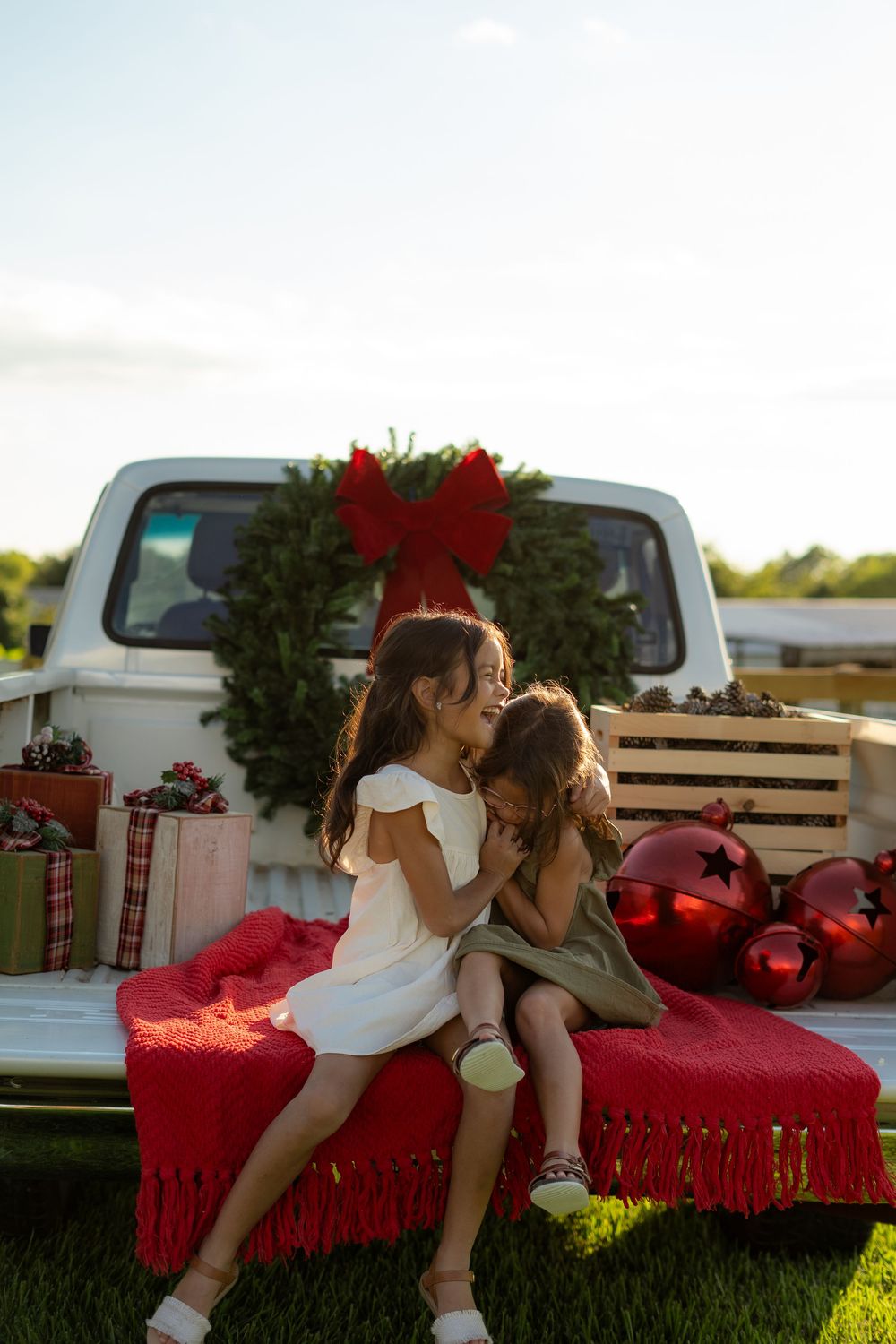 Family enjoying a festive Texas farm Christmas mini session, sitting on the bed of an old red Ford truck decorated with holiday greenery.