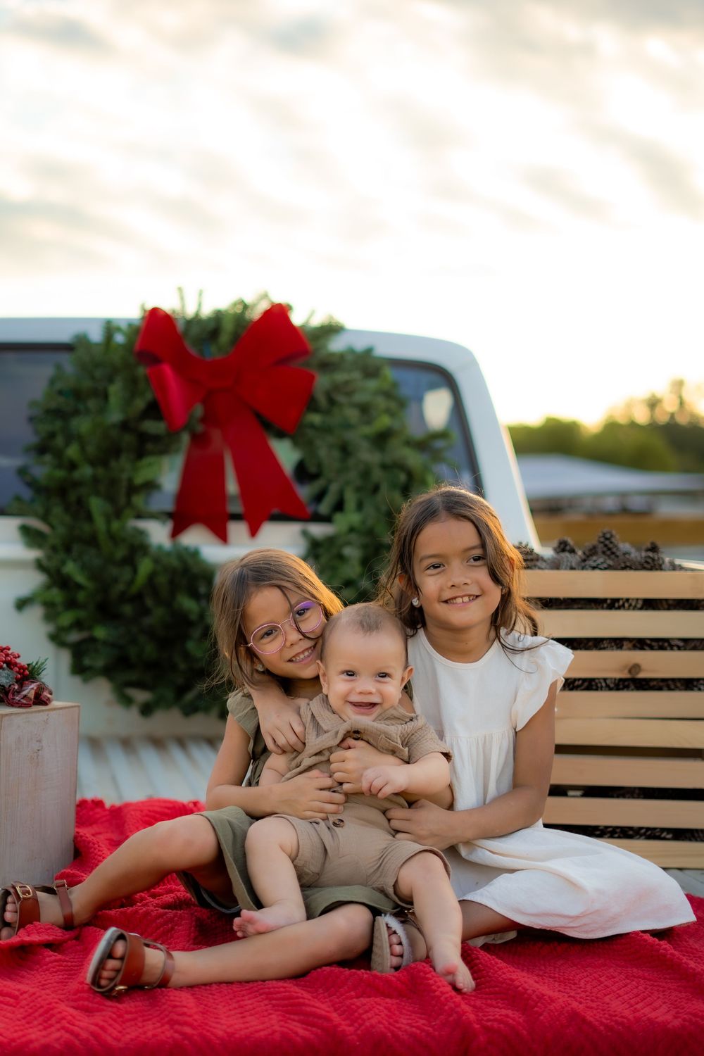Family enjoying a festive Texas farm Christmas mini session, sitting on the bed of an old red Ford truck decorated with holiday greenery.