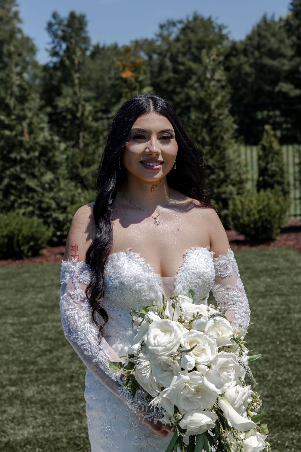 A stunning bridal portrait outdoors featuring an off-shoulder lace wedding gown and elegant white bouquet.