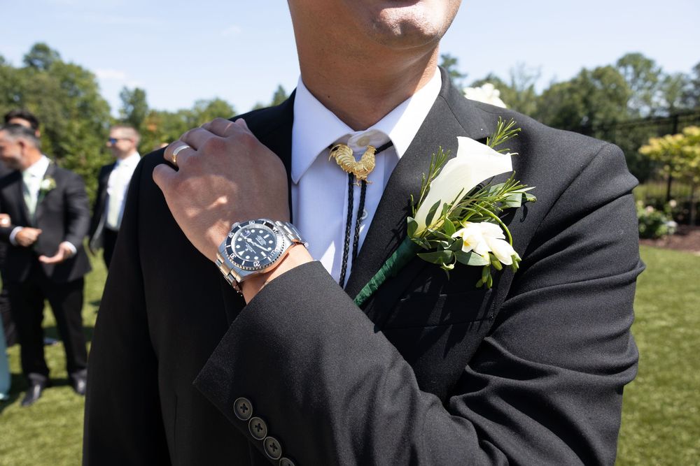Groomsmen in dark suits pose together outdoors at a formal wedding celebration.