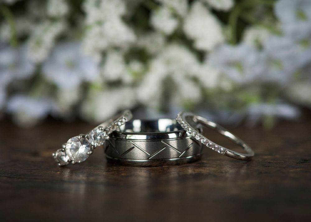 Close-up of wedding rings and jewelry against a blurred floral background.