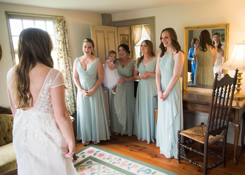 Wedding party in light blue bridesmaid dresses gathered in a sunlit getting ready room.