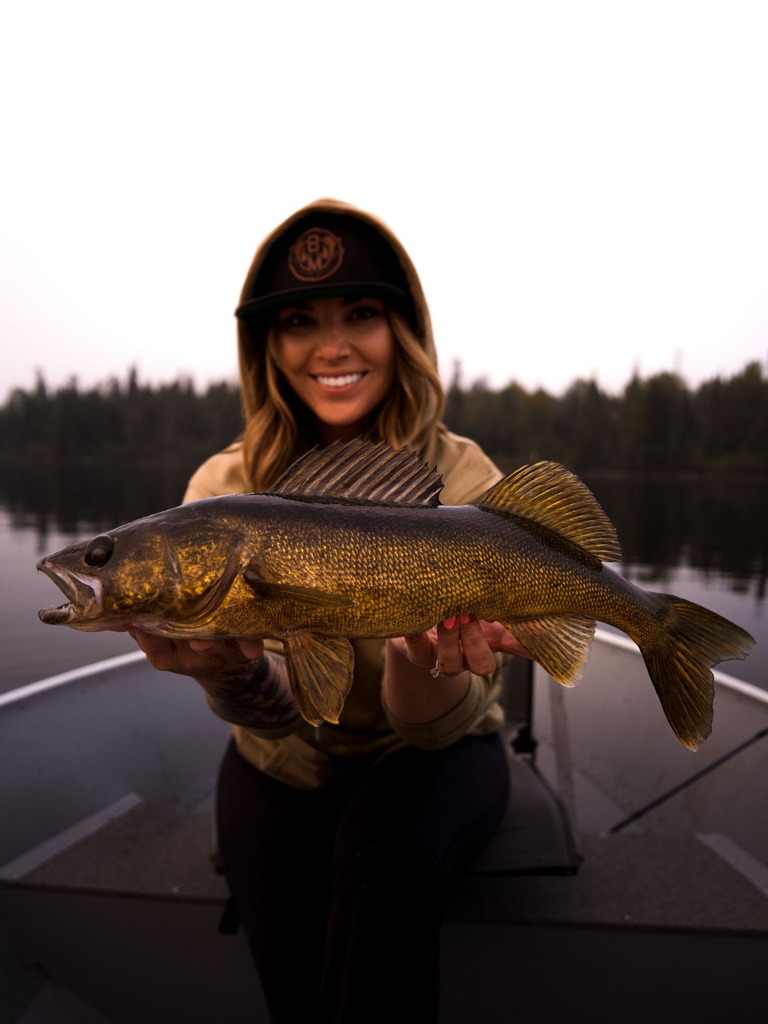 A successful angler displays a large walleye catch on a boat at dusk.
