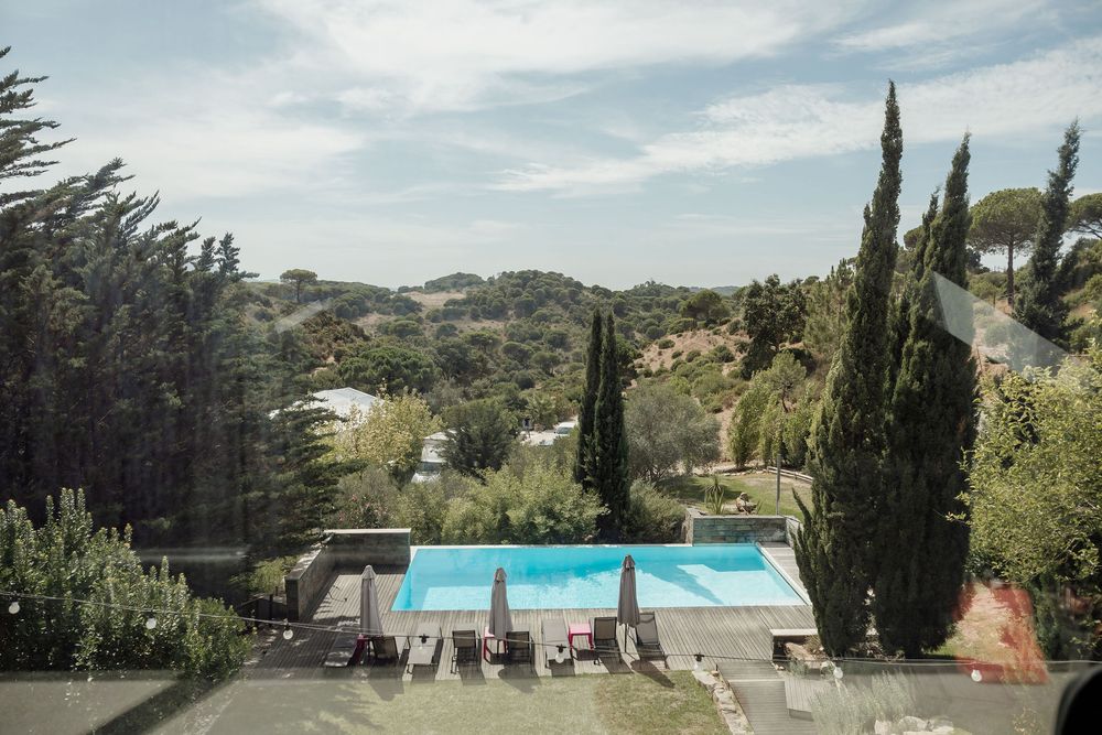 Panoramic view of a Mediterranean hillside villa with cypress trees and swimming pool overlooking scenic countryside.
