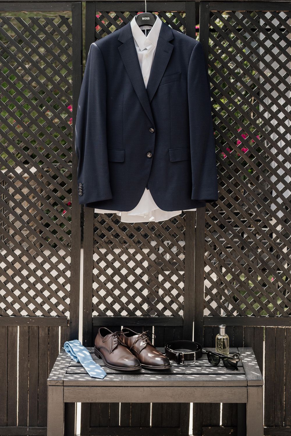 Navy suit jackets and brown dress shoes displayed on wooden lattice outdoor backdrop.