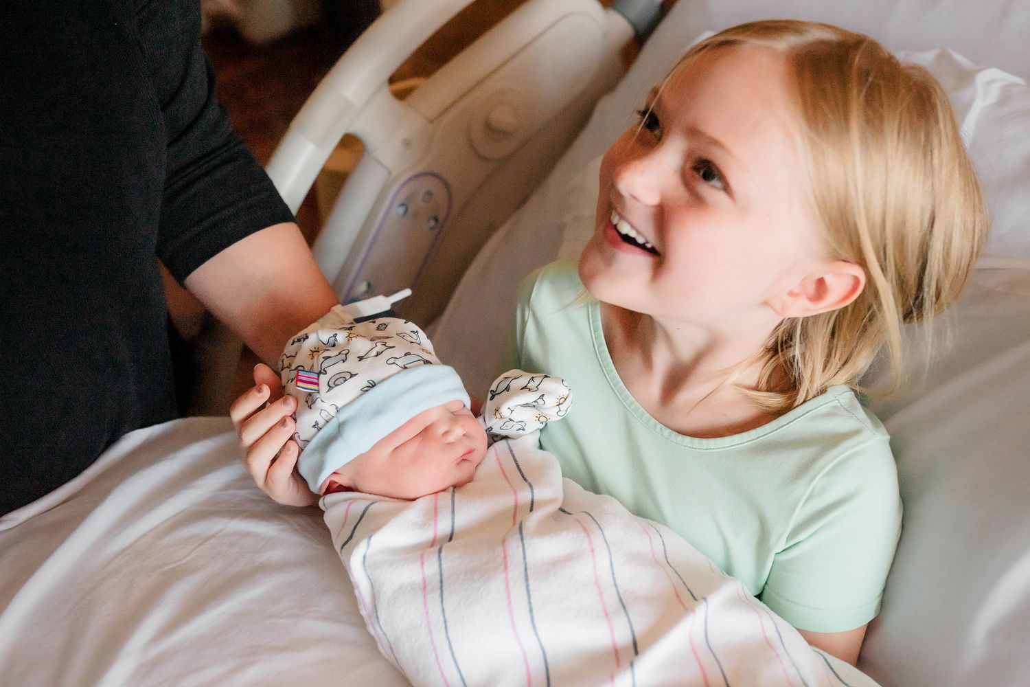Siblinghing holding newborn looking up at mom while smiling during fresh 48 session.
