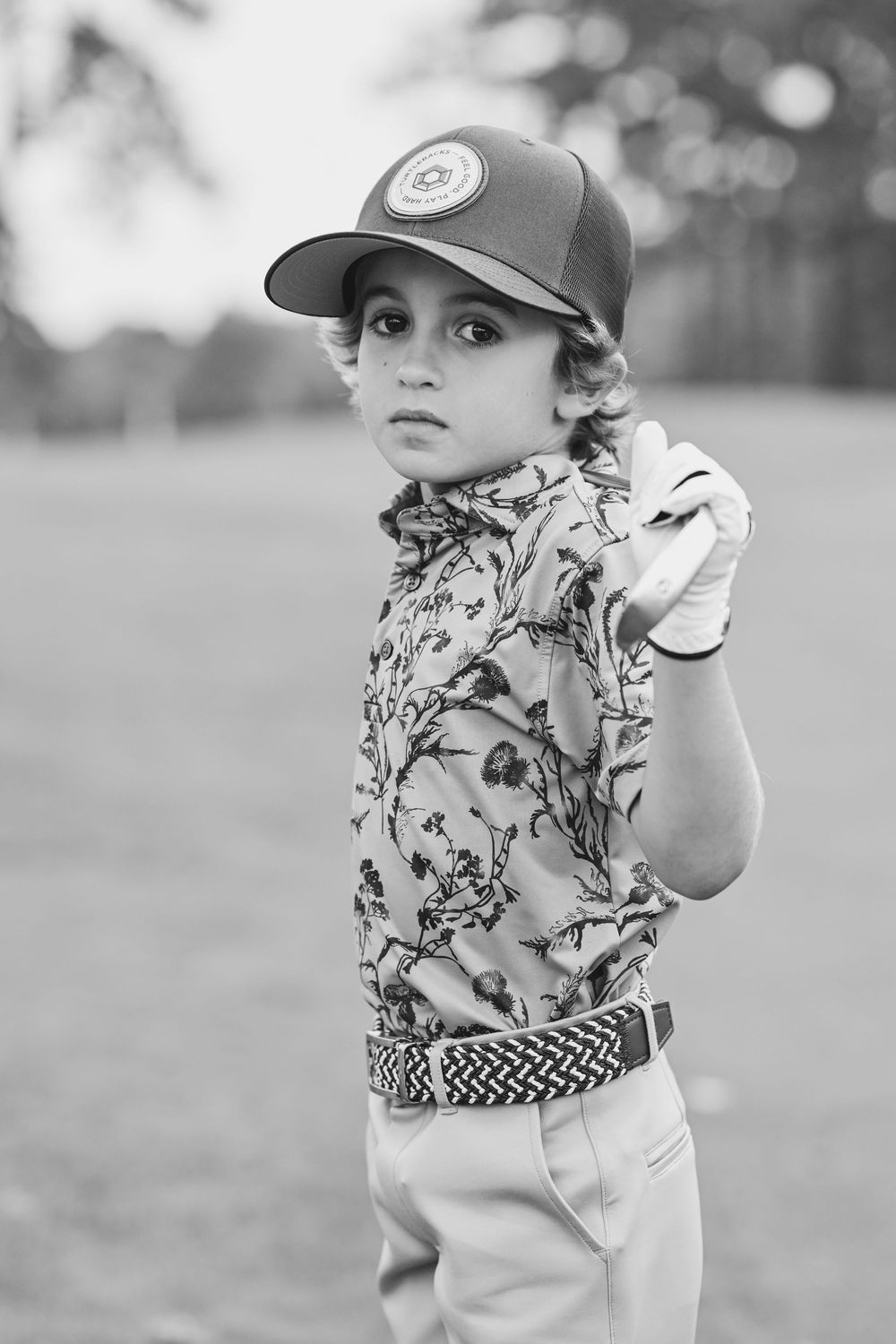 Young baseball player in patterned shirt and cap poses with bat.